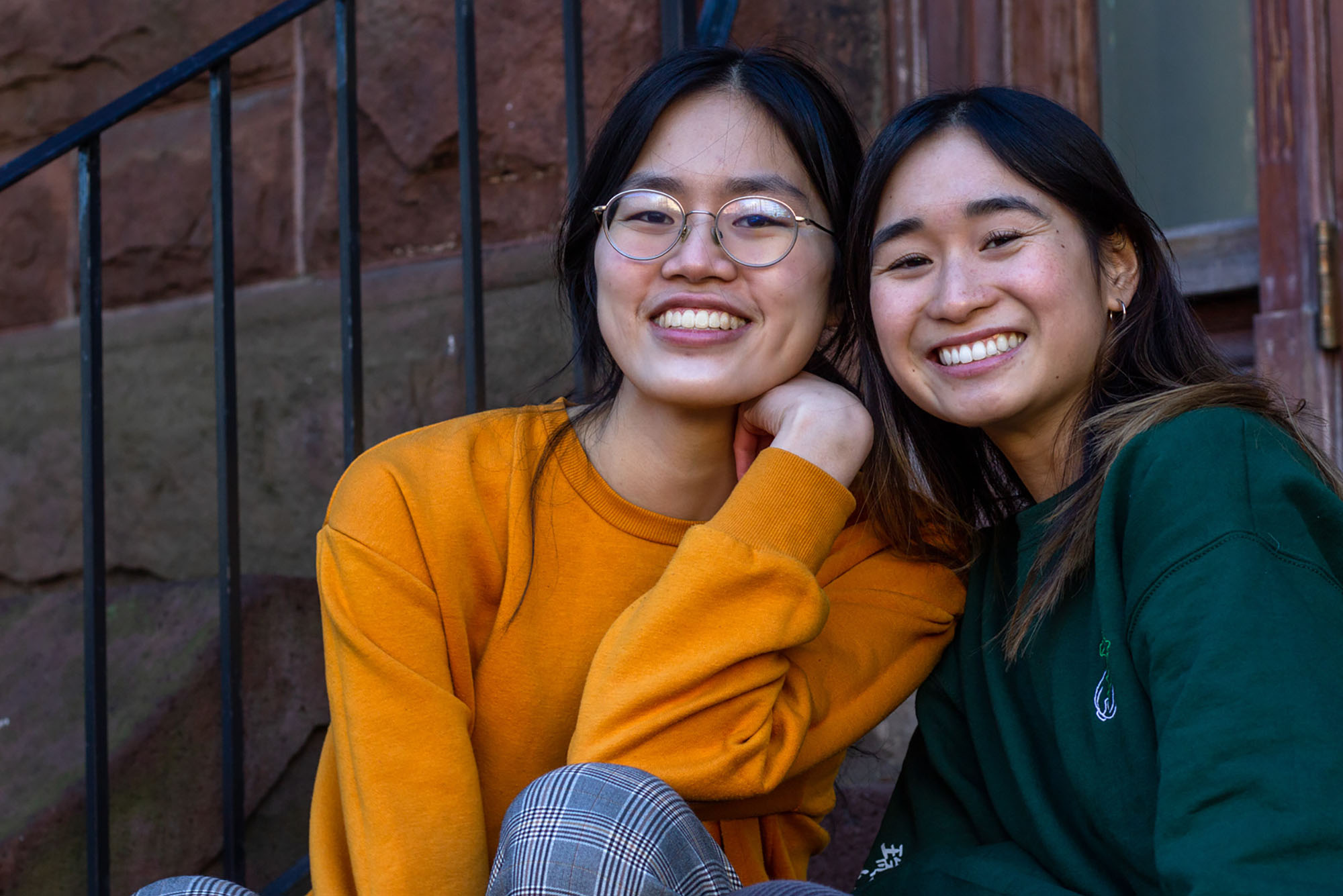 photo of Untangle Magazine’s creators Emily Wu (left) and Alyssa Yeh, 2 Asian American women. They sit on a brownstone stoop and smile to the camera.