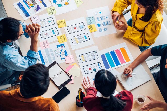 Top view photo of Asian ux developers and ui designers brainstorming about mobile app interface on a table with customer brief and color code in a modern office