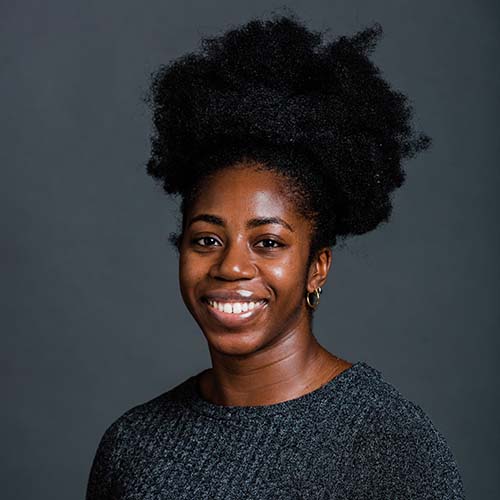 Photo of Gemma Acheampong, a young Black woman who smiles and wears a dark gray sweater.