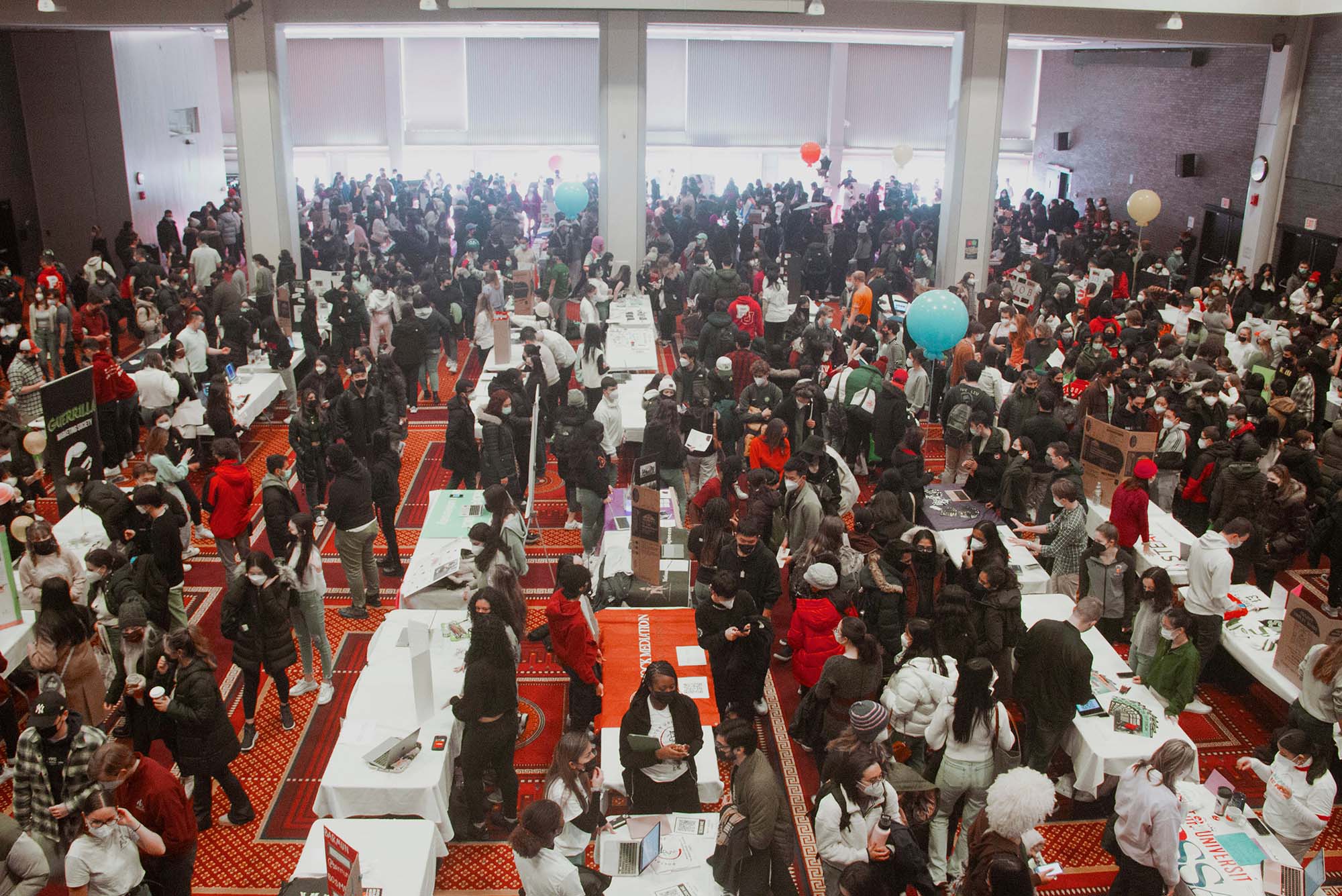 Photo of Splash 2.0, the Club Fair at the beginning of the second semester each school year, is held at GSU on Saturday, January 22, 2022. The GSU is filled with students, masked, many wearing winter coats, who stand and talk with students tabling with trifold boards and signs.