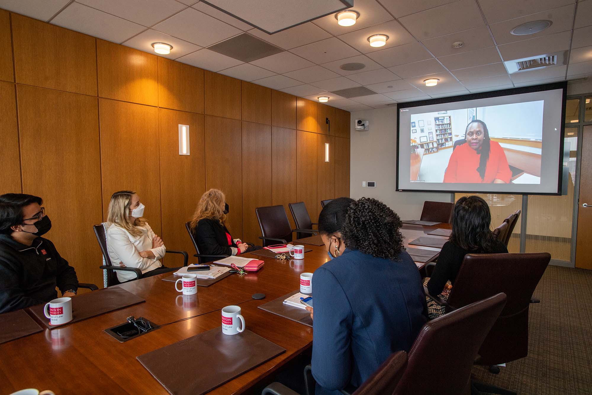 Photo of Julian Burlando Salazar (2L), from left, Clinical associate professor of law Naomi Mann, Director, A2J Clinic, from left, Associate Dean for Experimental Education Karen Pita Loor, lecturer and clinical instructor in the civil litigation justice program Jade Brown, and Marie Tashima (2L) watching LAW Dean Angela Onwuachi-Willig speak during the White House hosted eviction crisis summit Jan 28. The small group gathered to watch Onwuachi-Willig (on a projector screen, at the back right of the room) from the Alumni Boardroom at LAW.