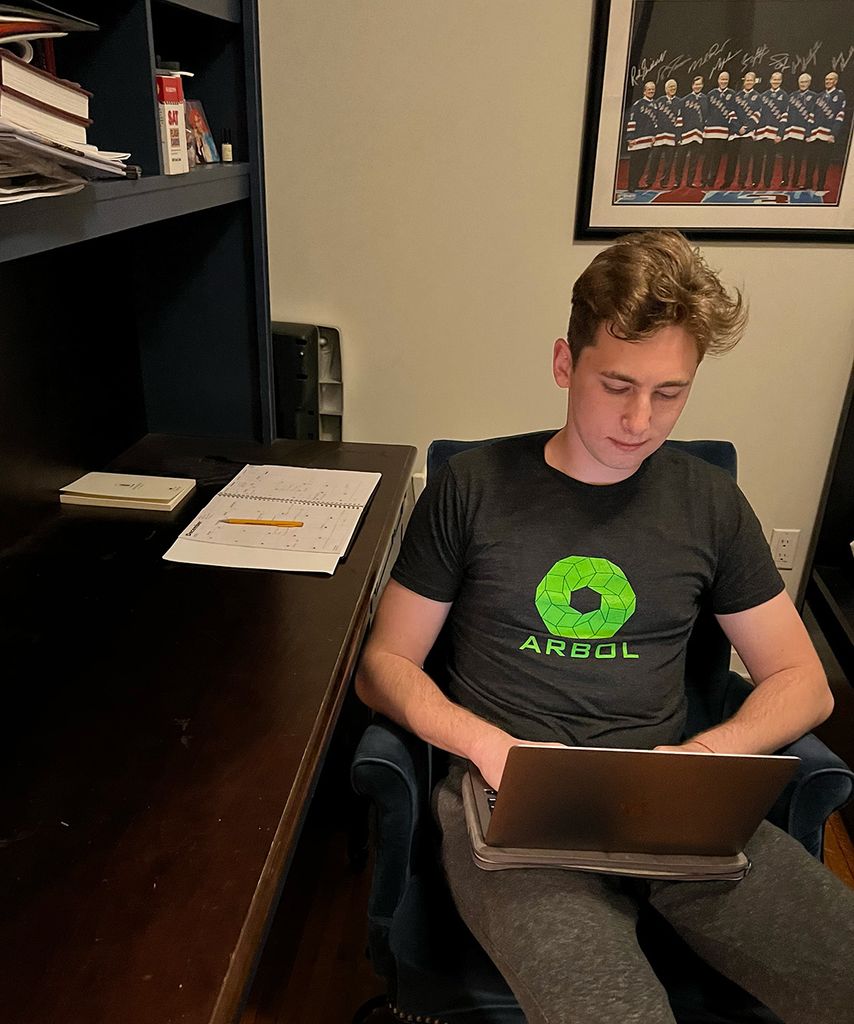 photo of Devin Hirsch using a laptop on his laptop as he sits turned away from a brown desk