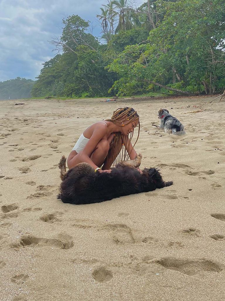 photo of Jaelyn Carr in a white swimsuit attending to a black dog lying on a sandy beach.