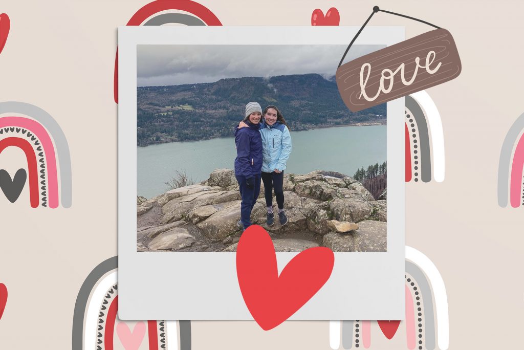 Image: Polaroid style photo of 2 women standing atop a rocky edge overlooking a large body of water. They wear winter gear and smile at the camera. Polaroid is placed on a tan background with a pattern of neutral style rainbows, a brown sign that reads "love", and a red heart