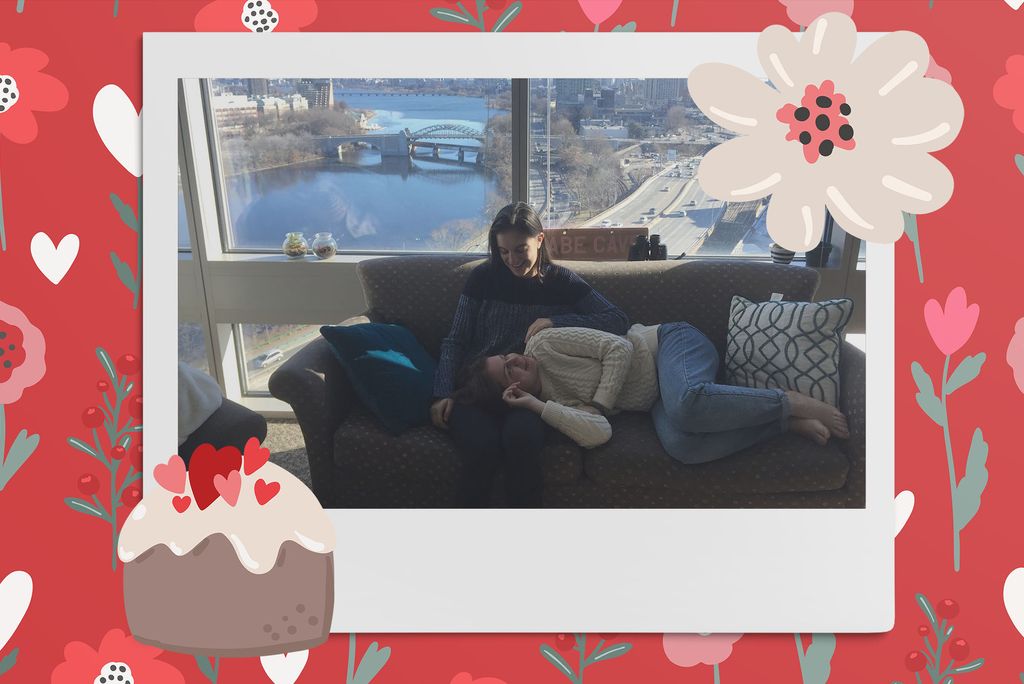 Image: Polaroid style photo of 2 women looking into each other eyes and smiling as one sits on the couch and the other lies down and rests her head in the other's lap. Polaroid is placed on a red background with a pattern of pink and red flowers and white hearts. Clipart of a tan flower and cupcake are placed near the polaroid.