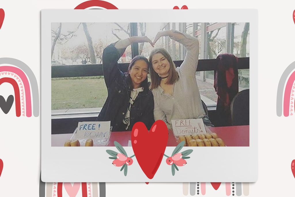 Image: Polaroid style photo of 2 women seated in the GSU and leaning towards each other with an arm overhead to create a heart with their bodies and smile at the camera. Polaroid is placed on a tan background with a pattern of neutral style rainbows, a brown sign that reads "love", and a red heart in the middle bottom of the polaroid