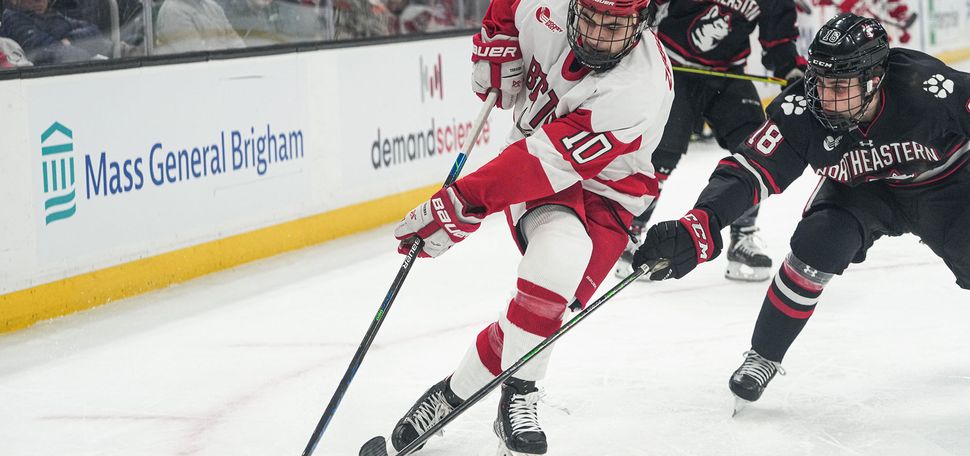 Photo of Nick Zabaneh (CAS’24) attacking against Northeastern’s Tyler Spott during the 69th Beanpot tournament championship game on February 14 at TD Garden. He skates forward with the puck as the Northeastern hockey player in a black uniform tries to intercept it.