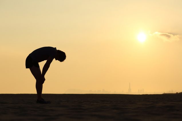 Photo of a silhouette of an exhausted sportsman at sunset with the horizon in the background