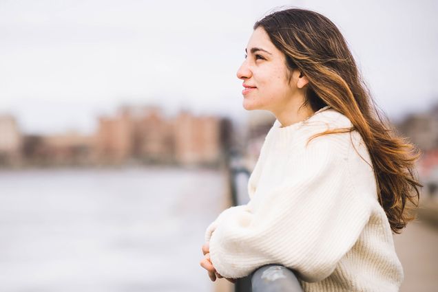 Photo of Sara Tavakoli (SDM’25). She is seen in profile, and leans on a railing along the Charles River looking out towards the water. She is light-skinned, has brown hair with highlights and wears a white sweater.