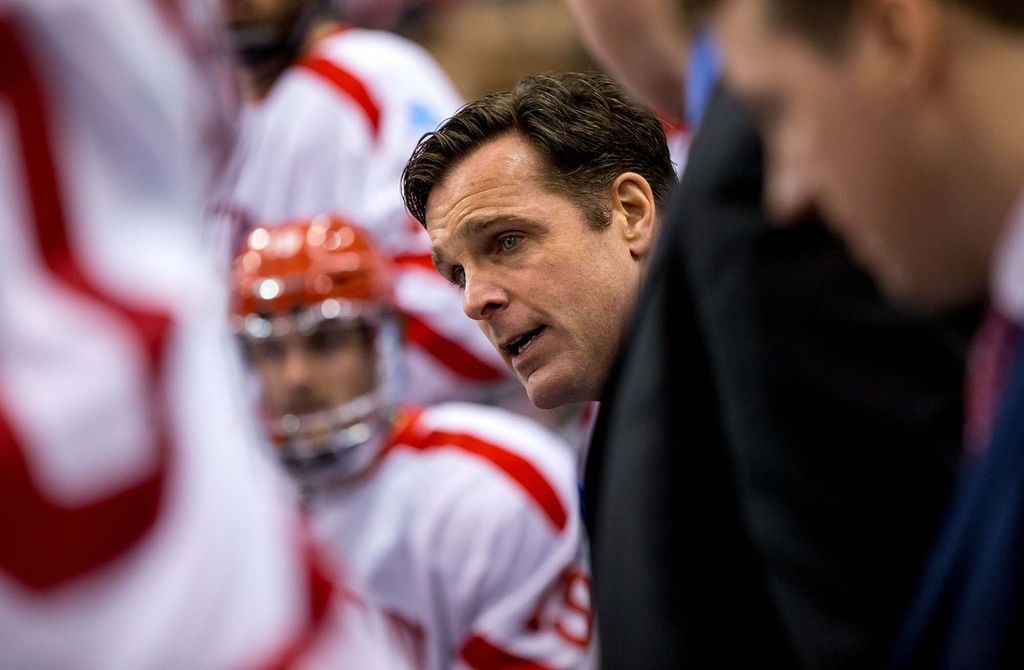 Photo of David Quinn (CAS’89), a former BU head coach, whose head is seen during a huddle with the men's hockey team. The players around him are blurred; he is White and has short brown hair.