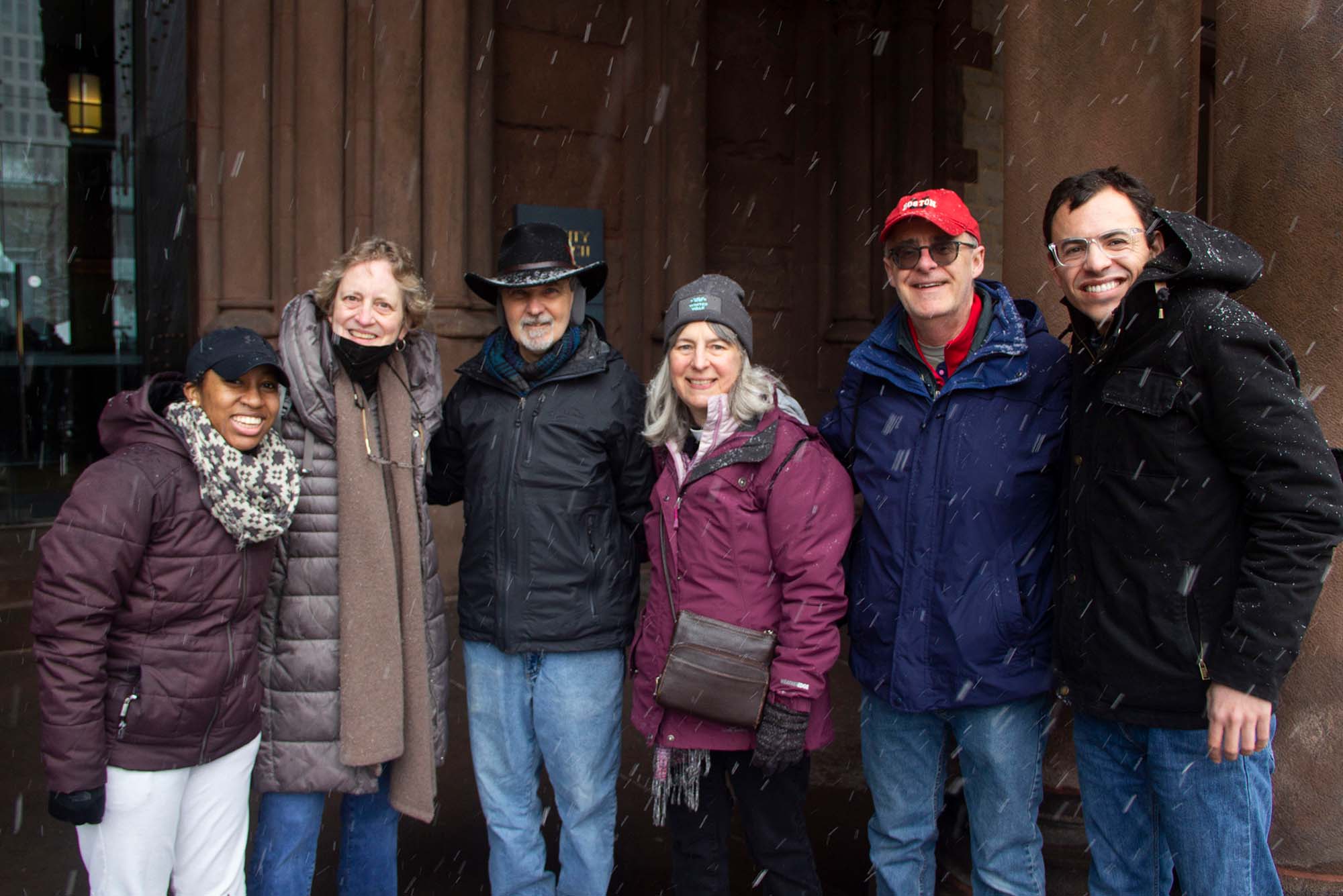 Photo taken during The Annual Winter Walk. The group of walkers from Boston University School of Theology pictured here participated in the event: Cynthia Perry (STH’24), from left, Dale Pinkham Cavanaugh (STH’24); John Clabeaux; Elise Feyerherm, Episcopal Mentor; Ray Joyce, Assistant Dean for Development; Johnathan Rocha (STH’24). The participants are bundled up in winter jackets, hats and scarves, and smile as snow falls.