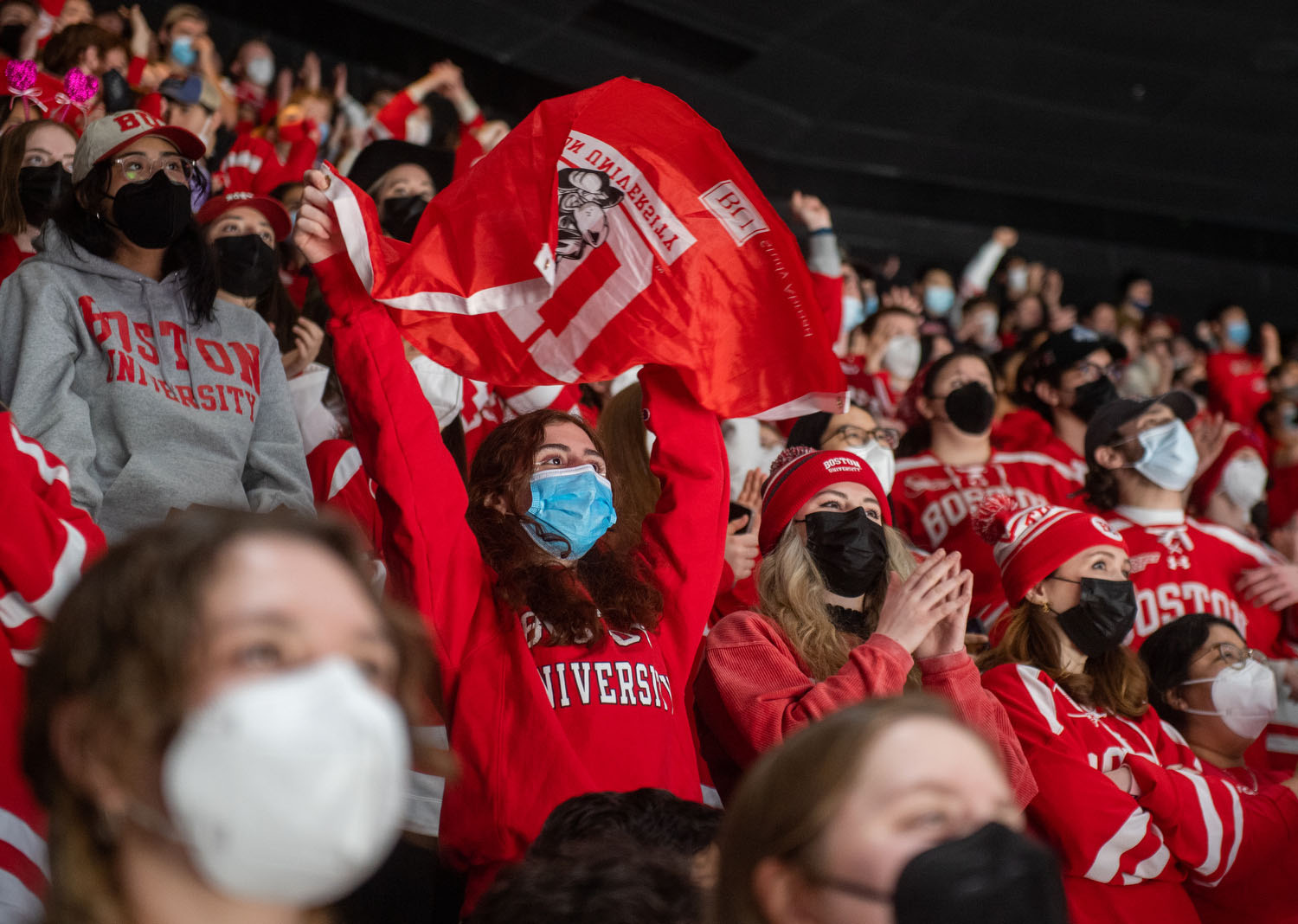 Photo of Mary Gogoladze (CAS’25) cheering from the Dog Pound during the Beanpot championship at TD Garden. She holds up a red BU flag and is surrounded by cheering fans wearing scarlet red BU gear
