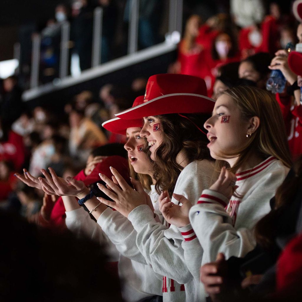 Photo of a group of female students during the Beanpot championship game Feb 14 at TD Garden. They wear cowboy hats and have BU temporary tattoos on their face. They smile, and clap their hands in celebrations, and are decked out with BU swag.