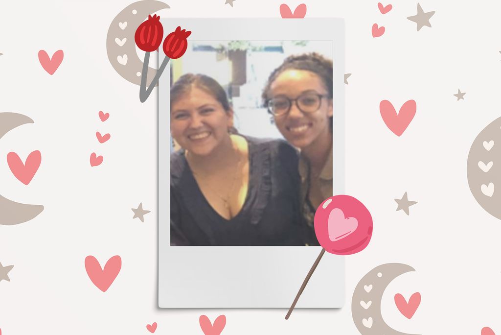 Image: Polaroid style photo of 2 women leaning towards each other as they smile at the camera. Polaroid is placed on a light tan background with a pattern of dark tan moons and pink hearts. A red flower and pink lollipop border polaroid.