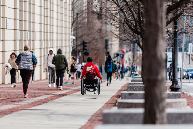 Boston University campus stock photography. Various students are seen walking up and down Commonwealth Ave. Student in center uses a wheelchair to move down the sidewalk.