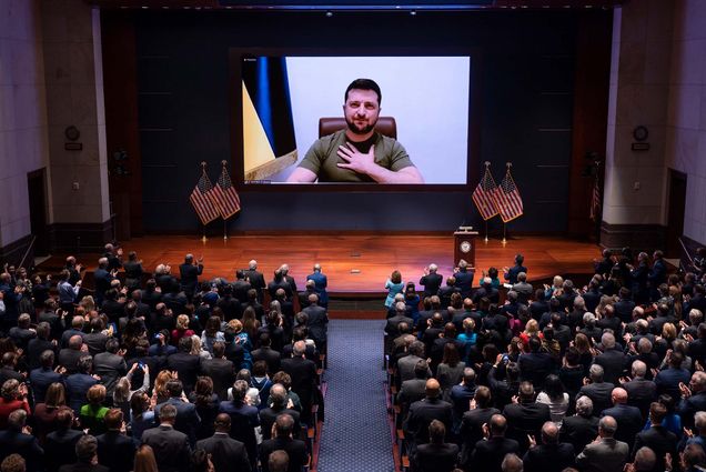 Photo of Ukrainian President Volodymyr Zelenskyy speaking to the U.S. Congress by video to plead for support. A Ukrainian man speaks on a large screen as people sit in auditorium seats to watch