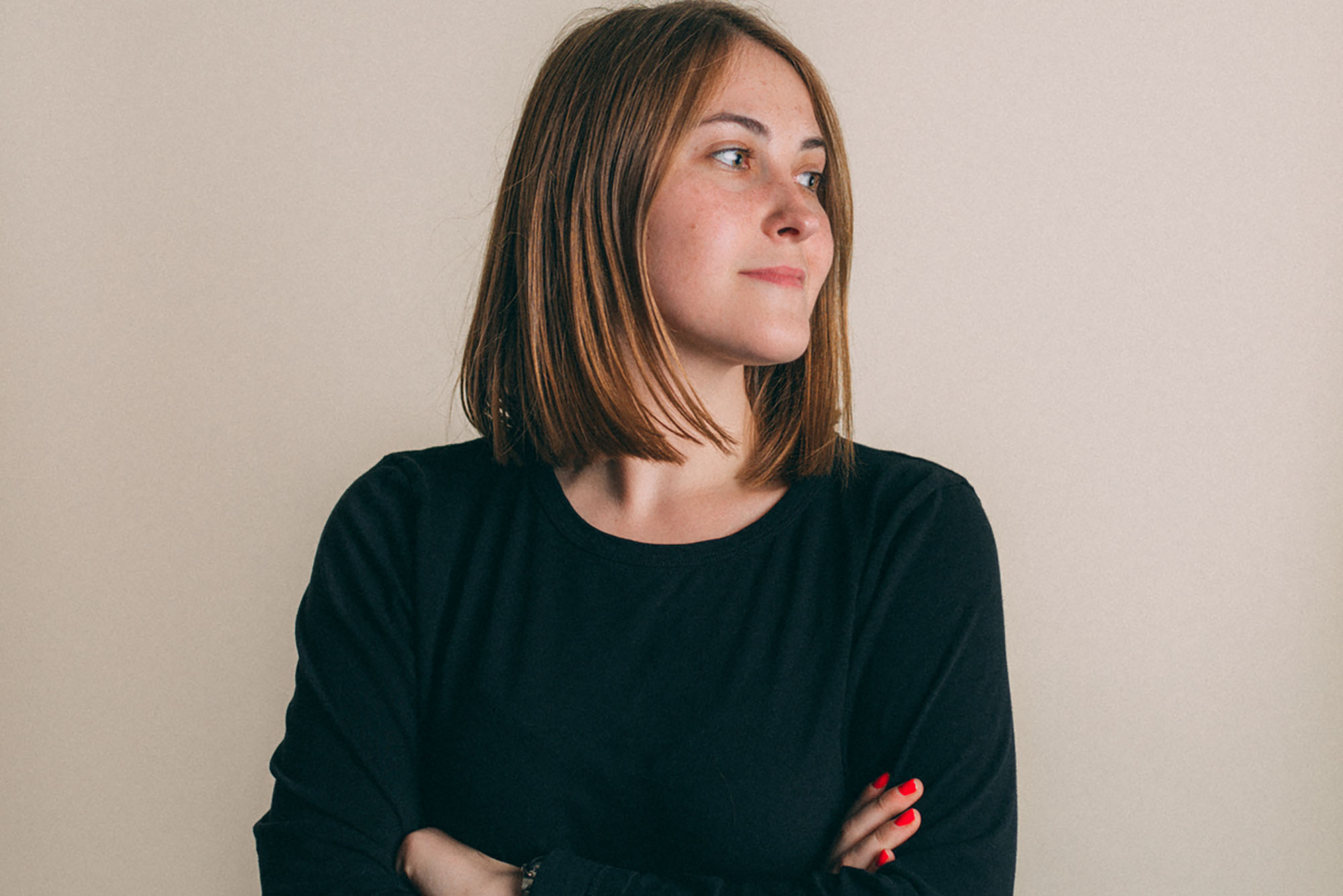 Headshot of Emma Johnson. A young white woman with short brown hair and wearing a long-sleeved black shirt smiles and looks off to the right with arms crossed.