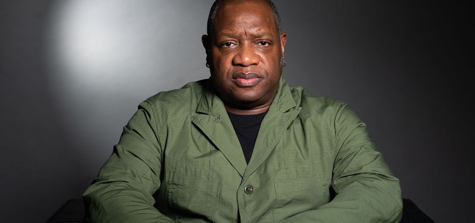 Louis Chude Sokei sits in front of a gray background in a green shirt