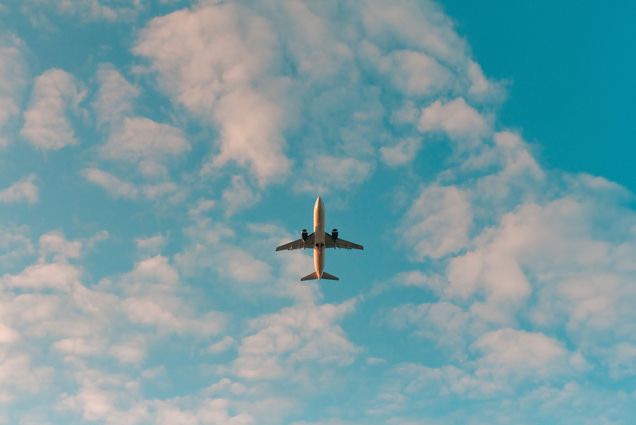 Photo of the underbelly of a plane flying overhead in a slightly cloudy sky