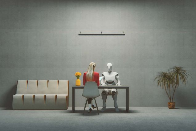 Photo of futuristic cyborg, with white and gray arms and legs, interviewing a job applicant, a woman with a red sweater and blonde hair. The image is 3-D generated. The cyborg and candidate sit at a desk in a sparse gray room.