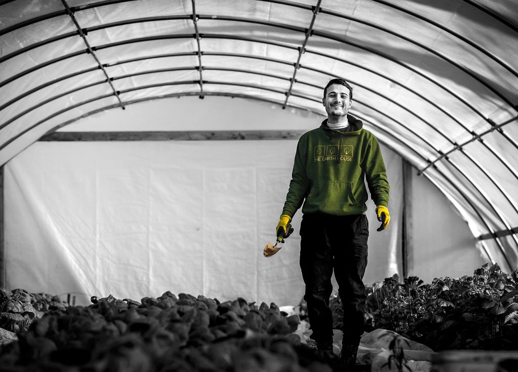 Black and white photo of Owen Woodcock (CAS’21), volunteering at an urban farm in Dorchester, Mass. His sweatshirt is colored green and his gloves are yellow.