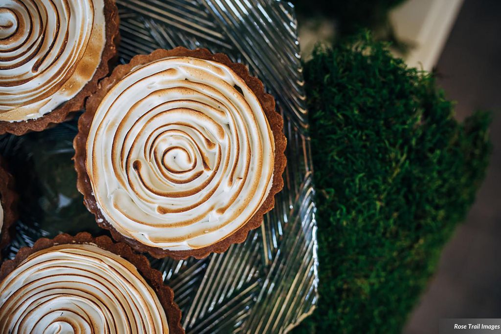 Overhead photo of Lemon rosemary meringue tarts. They sit on a clear plate with a patch of fake grass seen in the blurry background.