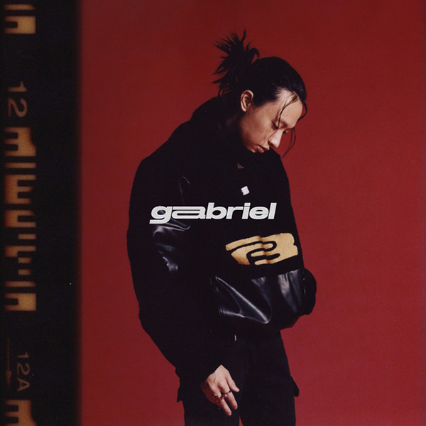 Album cover of Keshi's "Gabriel". Cover shows Keshi posing against a burnt red background and wearing an all black outfit. The word "Gabriel" is overlaid in white in the center.