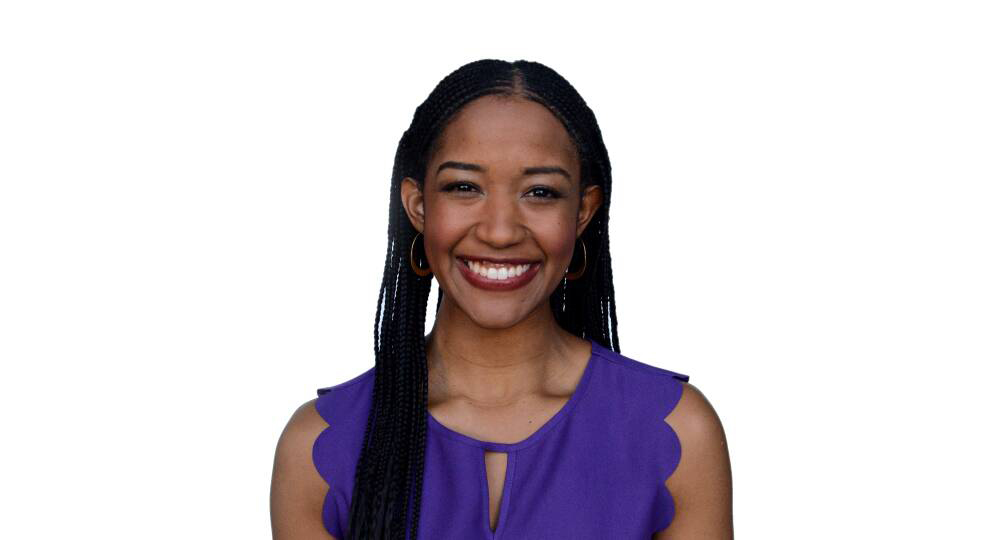 Headshot photo of Paris Alston, a young black women with long black micro braids, smiling straight ahead at the camera. She wears a flowery purple blouse and stands in front of a stark white background.