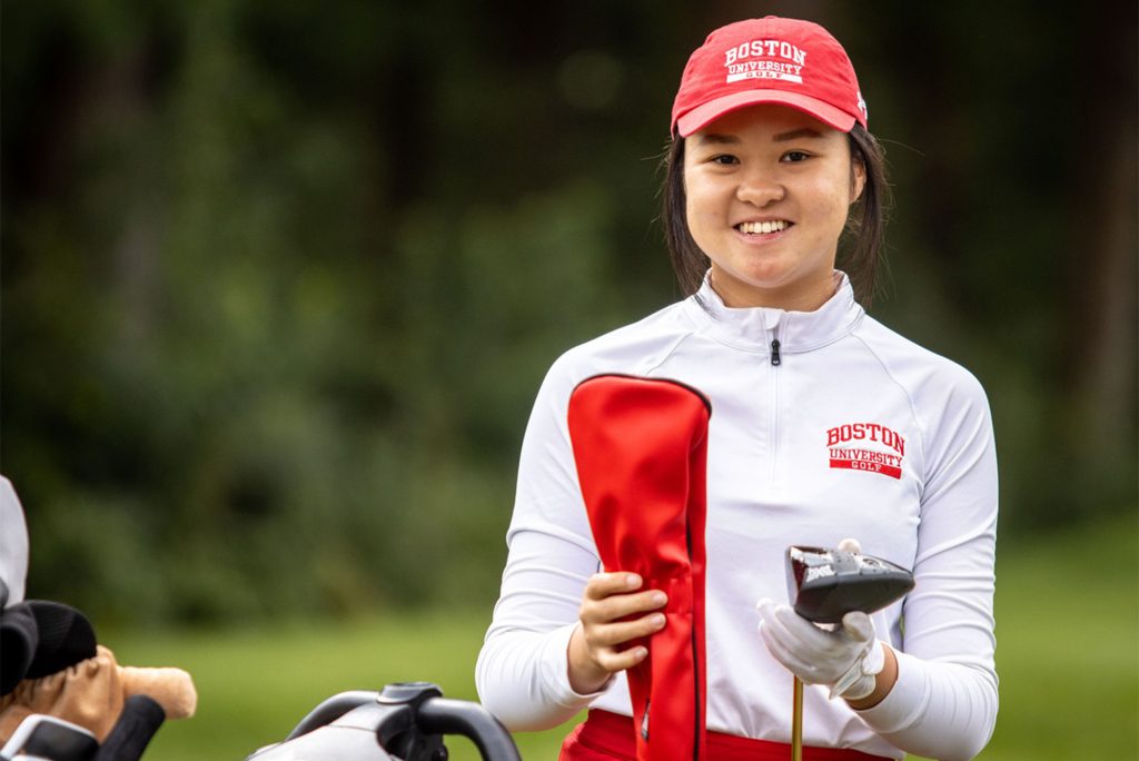 Hanako Kawasaki holds a golf club with a red headcover and smiles at the camera