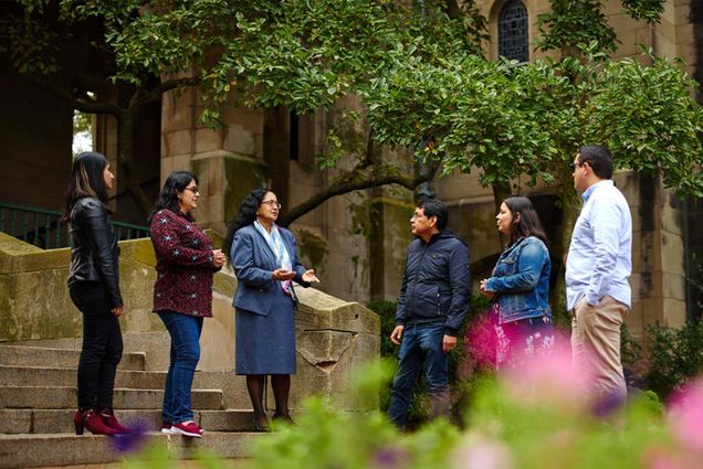 Multiple people stand in a semi circle in front of green trees on BU's campus in Boston MA