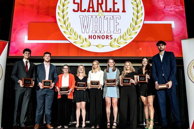 Photo of students dressed nicely, on stage, holding black, wooden plaques awards. Behind them on stage a large screen reads "Scarlet & White Honors"