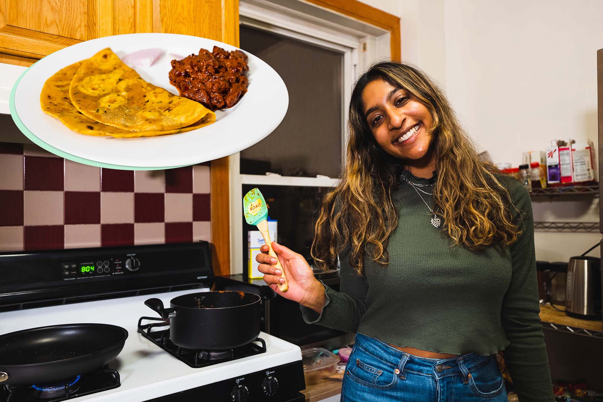 Photo of Neytra, a young Indian American woman with light brown skin and long brown, highlighted hair. She wears a green sweater and holds a spatula in her right hand. Behind her, you can see two black pots on a stove and a kitchen backsplash. At the top left of the photo is an image of the dish she cooked: curry made with red kidney beans and pureed tomatoes and flavored with spices like cloves, tumeric, and cinnamon with a side of roti. White play button is overlaid.