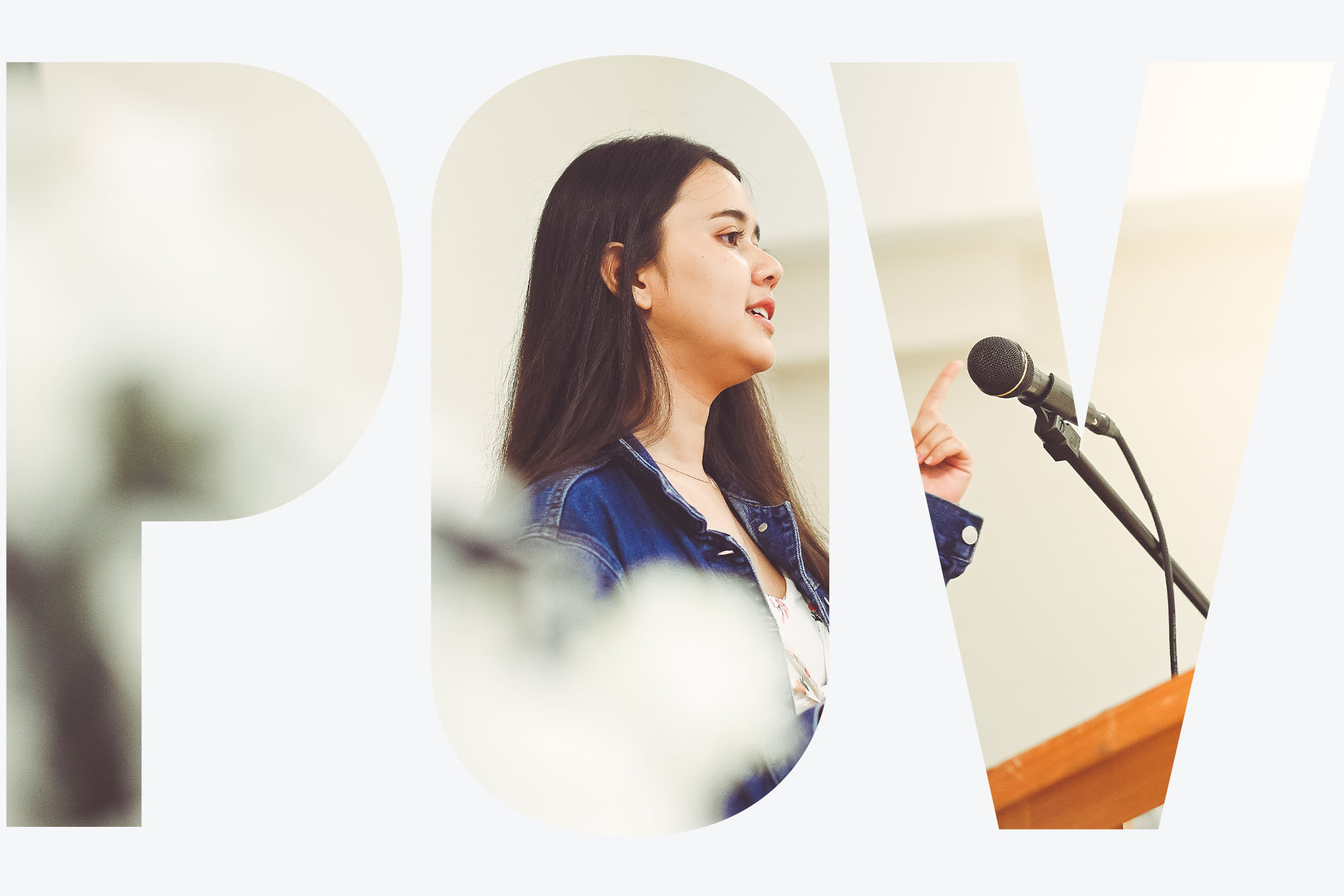 Photo of a young woman, either a high school or college student with brown hair, wearing a jean jacket, speaking at a wooden podium into a microphone. She gestures with her left hand and appears to be mid-speech. Overlay reads "POV"