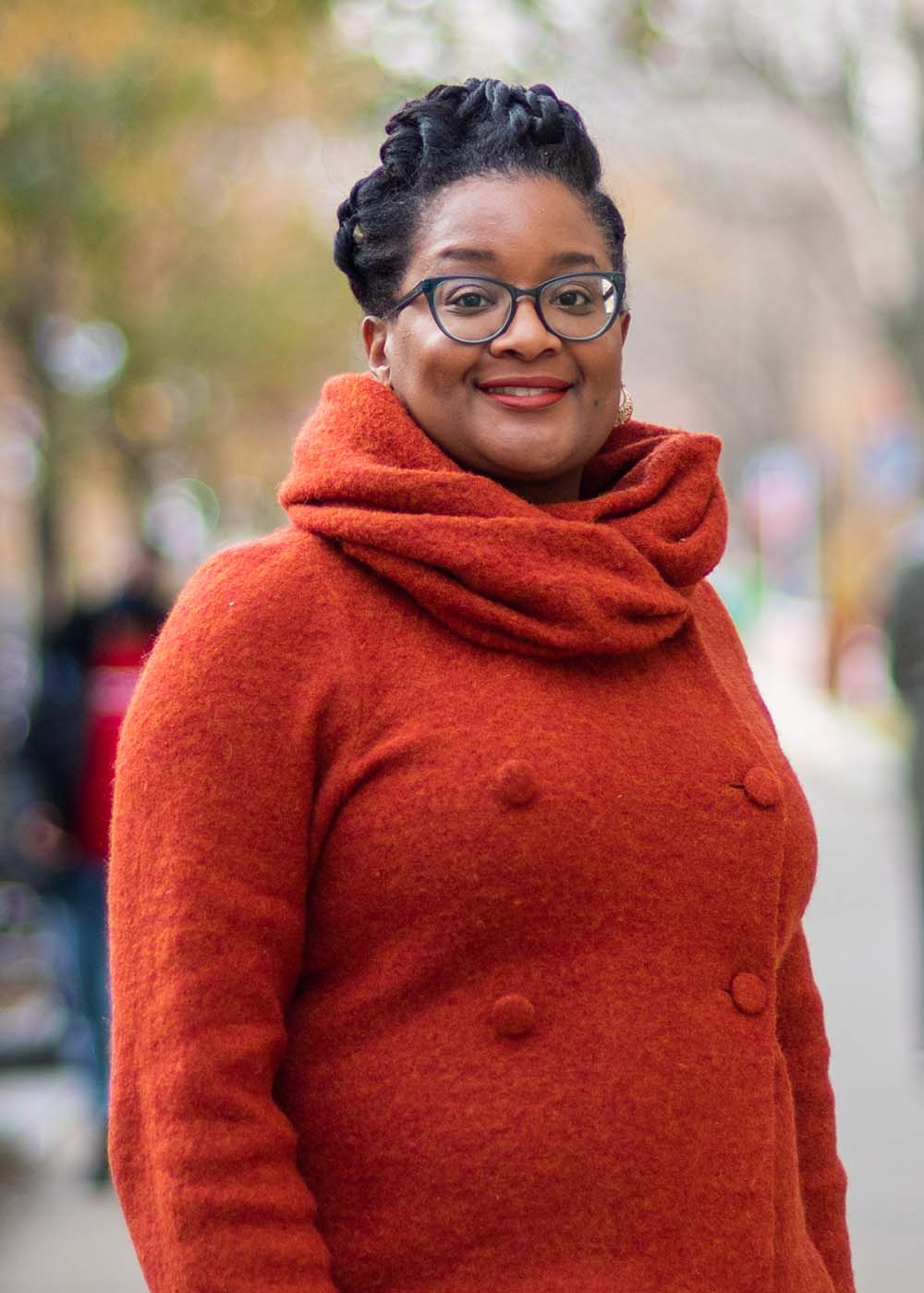 Photo of Malika Jeffries-EL, a College of Arts & Sciences associate professor of chemistry and associate dean of the Graduate School of Arts & Sciences, a Black woman wearing an orange sweater and black pants, smiling as she stands on a side walk along Comm Ave.