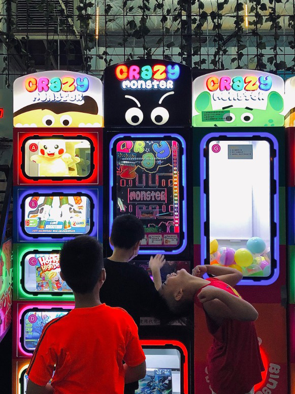 Photo of three young boys in an arcade center at night. They stand in front a bright game as one plays, one looks on, and the other shows an expression and feeling of excitement