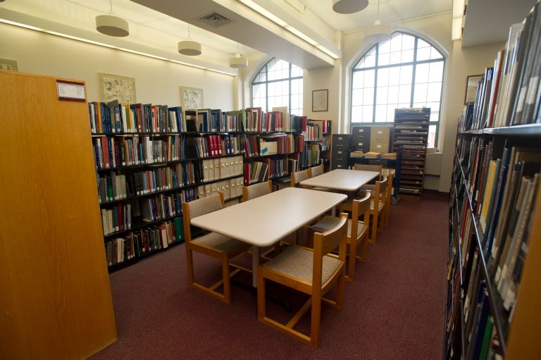 Photo: The interior of a small library, with shelves of books lining the walls where arched windows let in light.