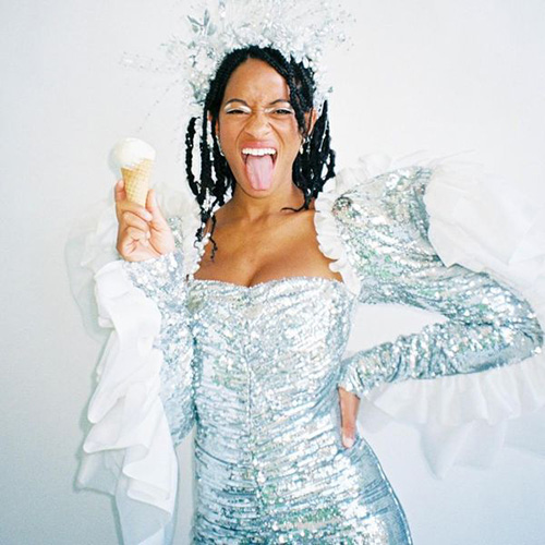 Album cover for Kilo Kish's "American Gurl". Cover is a photo of Kilo Kish posing with eyes closed, tongue out, right hand on hip, as she holds a vanilla ice cream cone in her left hand. Kish wears an elaborate silver dress and headdress reminiscent of the Statue of Liberty.