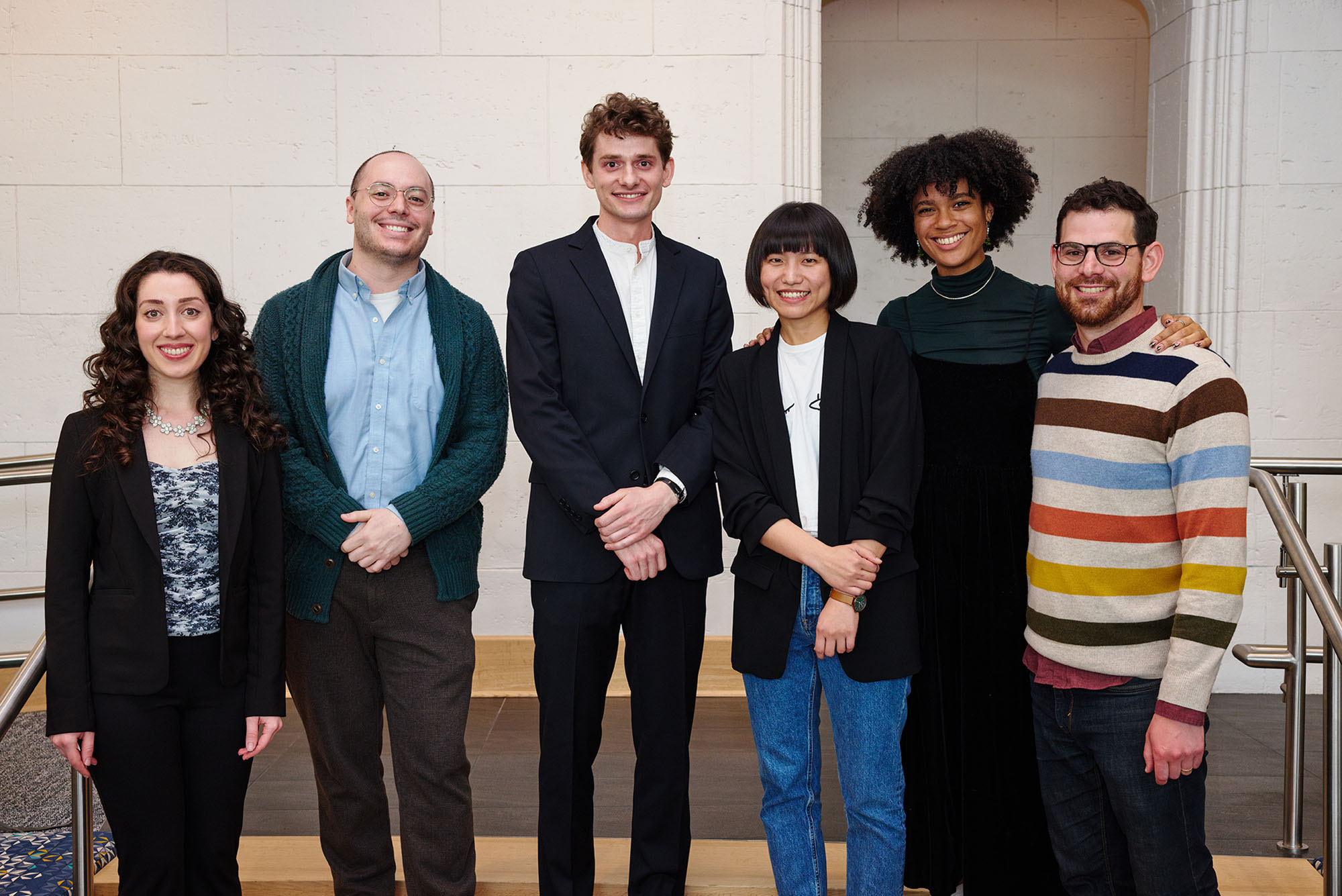 Photo of this year’s Kahn winners (from left): Savannah Panah (CFA’22), music and vocal performance (from left), Devon Russo (CFA’22), music and vocal performance, grand prize winner Gavin Fahey (CFA’22), painting, Chen Peng (CFA’22), painting, Mya Ison (CFA’22), theater arts and performance, and Noah Putterman (CFA’22), directing. A group of students dressed in business casual wear stand in a line and pose for the camera.