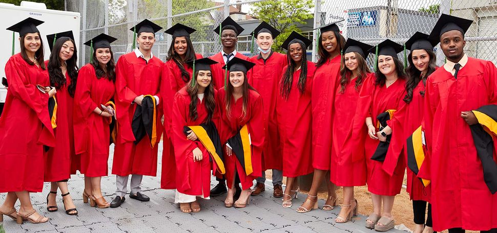 Photo of Graduate Medical Sciences master’s degree candidates before their convocation ceremony. A diverse group of young adults stand in a group wearing red caps and gowns and black caps on a sunny day.