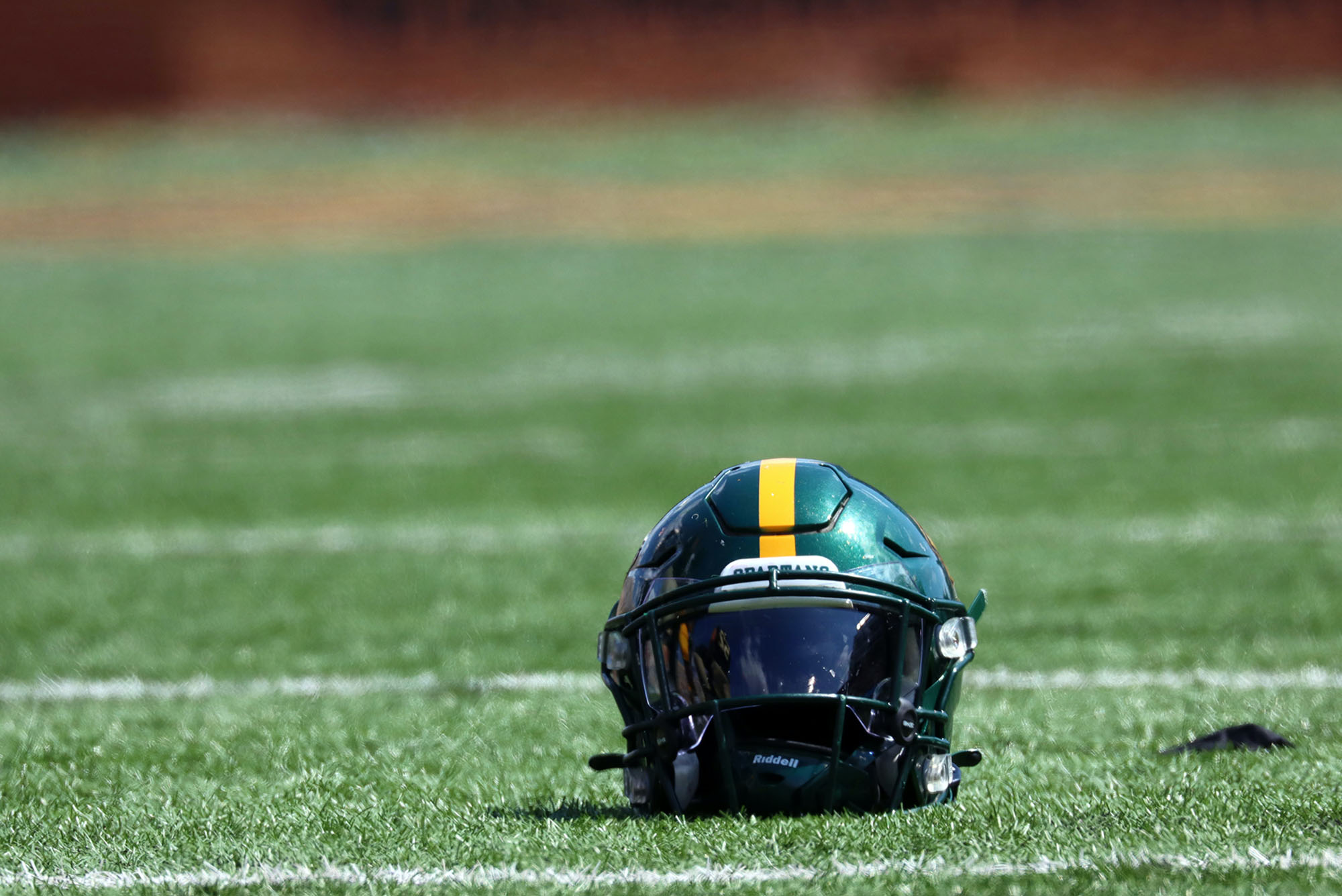 Photo of a green and yellow helmet sitting on a green turf football field.