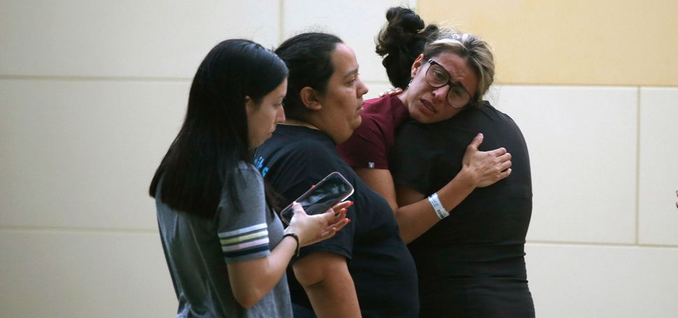 Photo of the members of the community of Uvalde, Tex., mourning after a deadly school shooting at Robb Elementary School. In the photo, four women presumably Latinx women are seen, mostly from the side. One woman hugs another, her face is filled with tears. She has blonde hair and wears glasses.