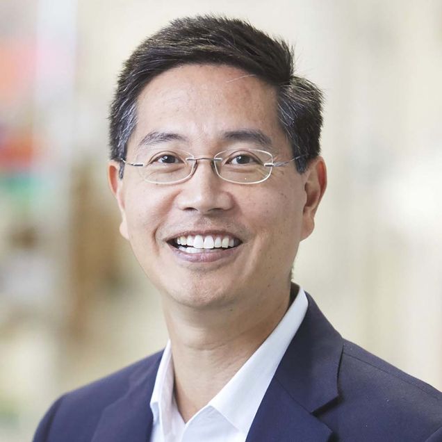 Headshot of Chris Chen, a middle-aged Asian American man with glasses. He smiles and wears a blue suit.