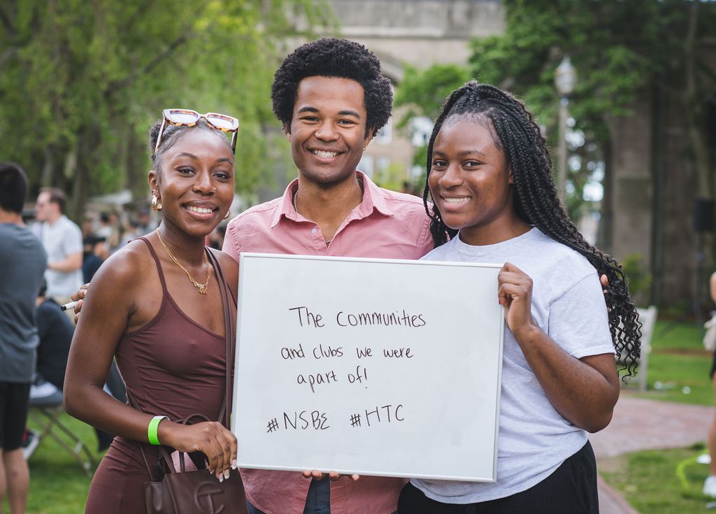 Photo of (Left to right)Samantha Garwood (CAS 22) , Ethan Strauther (ENG 22) and Chidera Osuji (SAR 22). They stand together and hold a sign that reads "The communities and clubs we were a part of! #NSBE #HTC". 