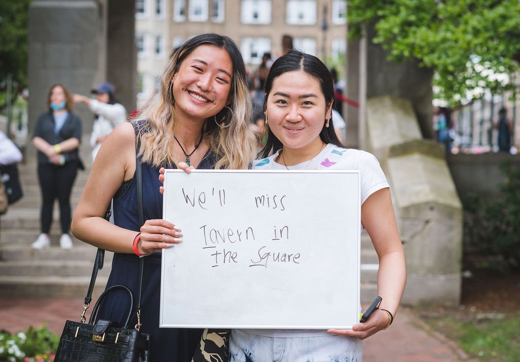 Photo of Jiamu Sun (CAS 22) and Natasya Tandra (CAS 22) , 2 young women. They stand and pose holding a sign that reads "We'll miss Tavern in the Square". 