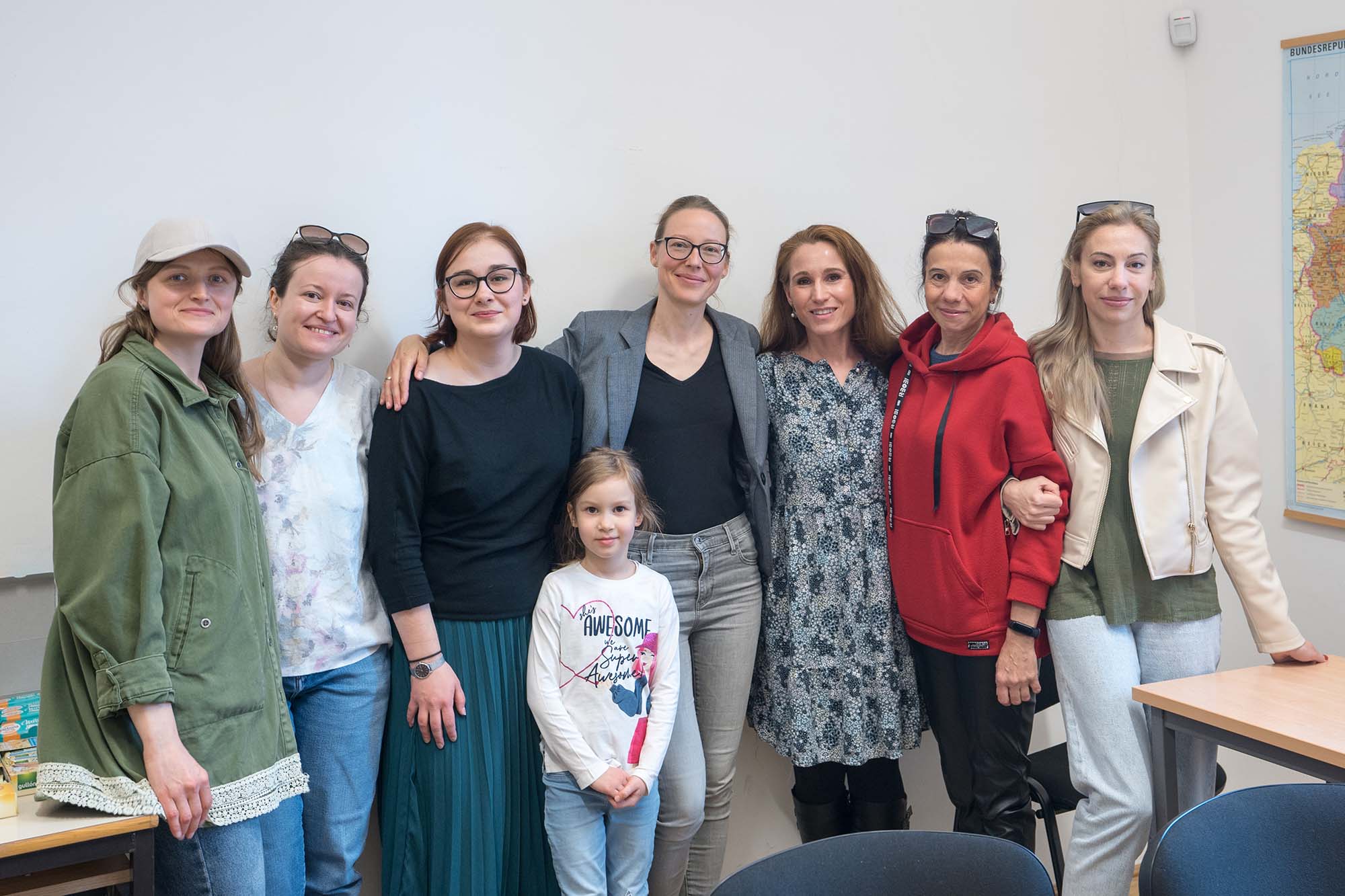 Photo of(from left) Yuliia Terentieva, Kristina Kocyba, Theodora Goss, and four Ukrainian refugees who are in Goss’s intermediate English class, and a little girl. They all stand in a line with arms over each other shoulders as the child stands in front in the center.