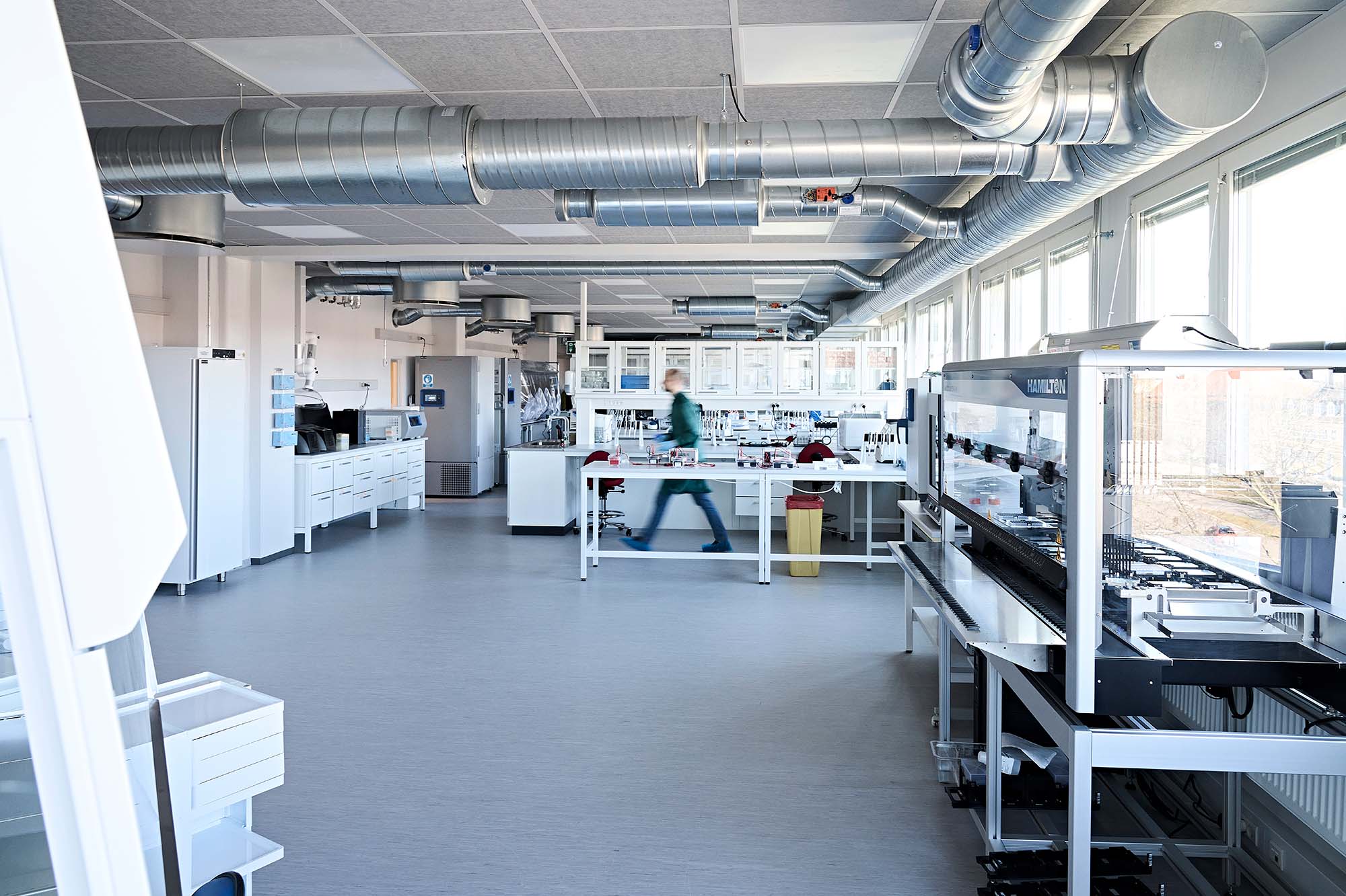 Photo of the newly opened GMO2 laboratory. Photo shows a bright, large lab, with a blurry person caught mid-walk in the center.