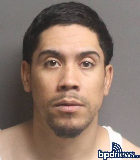 Photo of suspect Edwin Fantauzzi. A Hispanic-appearing man with short black hair, thing mustache and beard, and wearing a white tank top stands in front of grey wall with a neutral expression.
