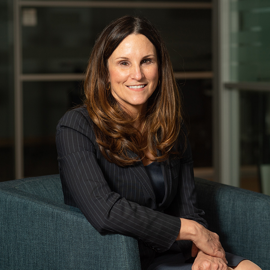 Photo of Erin Duffy, CARB-X's chief of research. Duffy sits in a blue arm chair and is turned towards the camera. She wears a navy blazer and skirt.