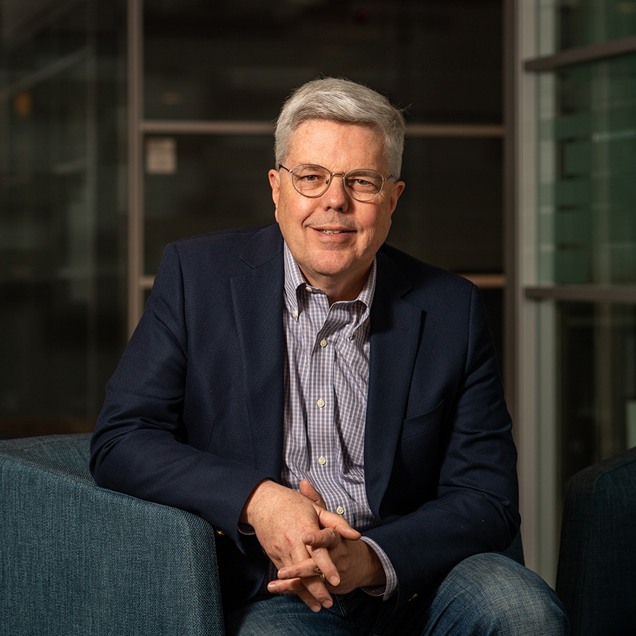 Photo of Kevin Outterson, Executive Director, CARB-X. Outterson sits in a blue armchair with hands folded in front of him as he poses fort he camera. He wears a navy blazer, jeans, and a light purple collared shirt.