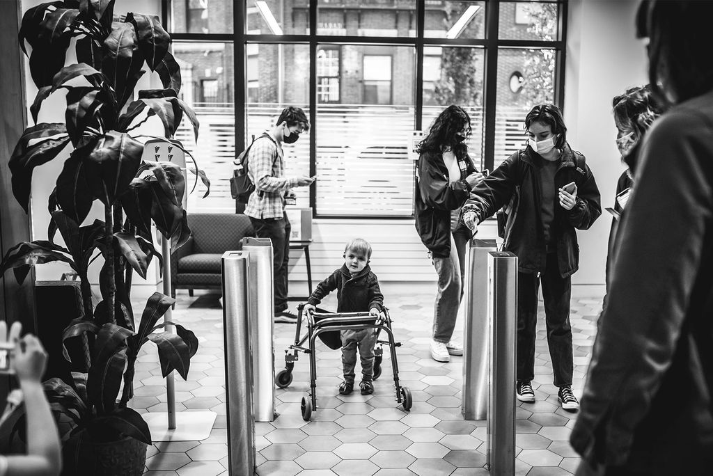 A small child with a walker is seen in a modern hi-rise lobby. Griffin has CHARGE syndrome. Lacking an inner ear structure, and therefore no natural balance system, he uses a walker to get around, but is learning how to walk unassisted. “He’s an incredibly joyful, smart, happy, funny kid,” his mom says.